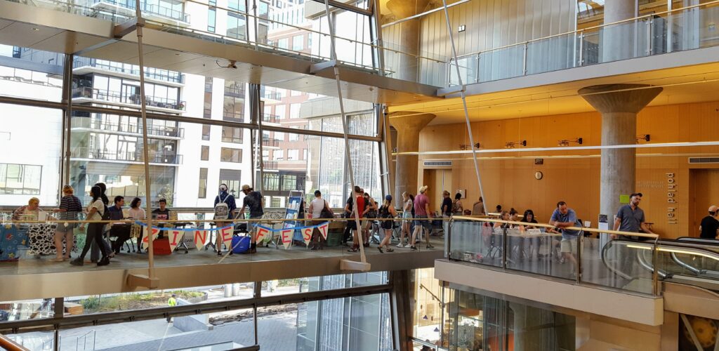 People shop at a series of tables set up in a very airy, window-filled room.
